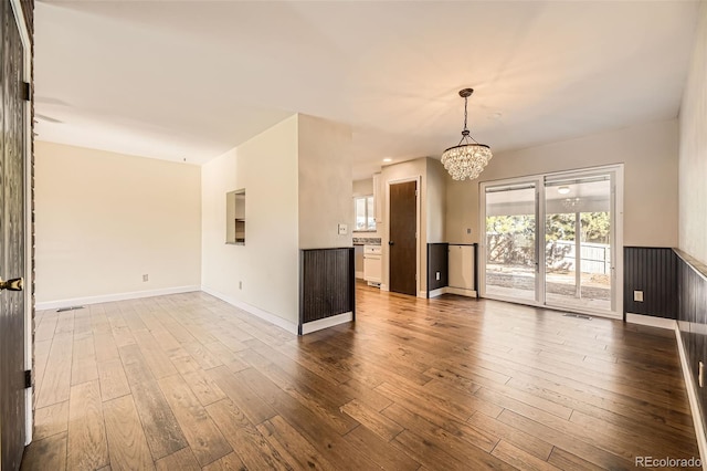 unfurnished living room featuring an inviting chandelier, visible vents, baseboards, and wood finished floors