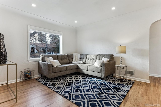 living area featuring arched walkways, visible vents, baseboards, and wood finished floors