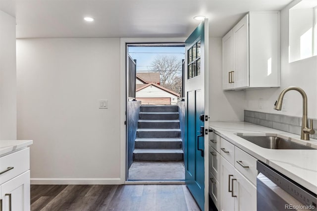 kitchen featuring a sink, light stone counters, stainless steel dishwasher, white cabinetry, and dark wood-style flooring