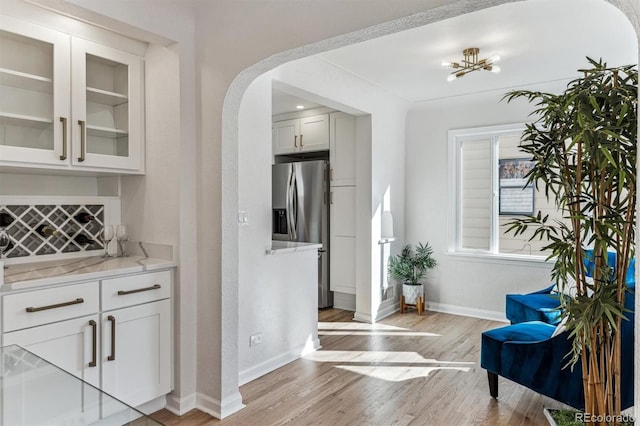 bar with baseboards, light wood-type flooring, stainless steel fridge with ice dispenser, arched walkways, and tasteful backsplash