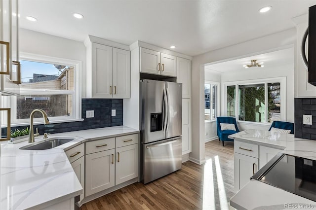 kitchen featuring light wood finished floors, backsplash, light stone countertops, stainless steel fridge with ice dispenser, and a sink