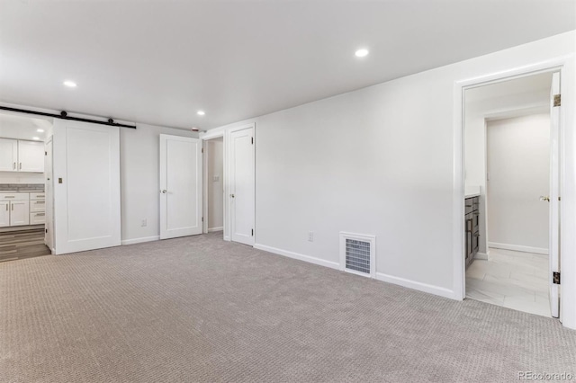 unfurnished bedroom featuring recessed lighting, visible vents, carpet flooring, and a barn door