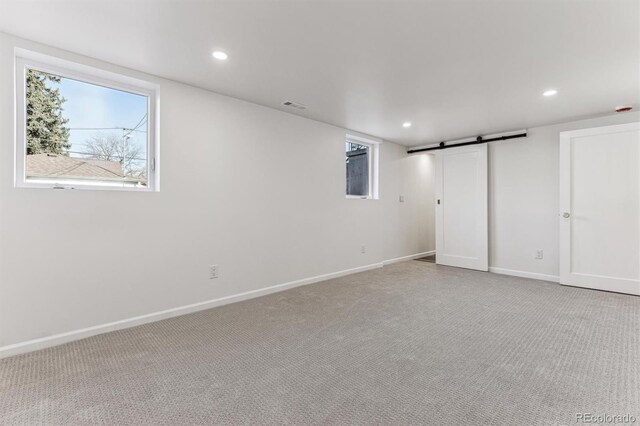 basement featuring a barn door, carpet, visible vents, and a healthy amount of sunlight