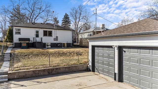 view of side of property featuring a fenced front yard, a shingled roof, and a garage