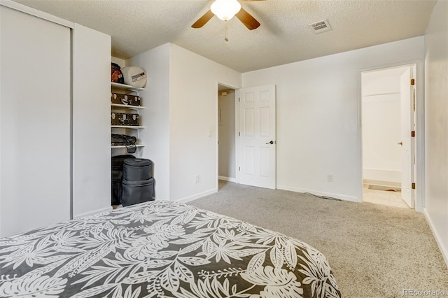 carpeted bedroom featuring ceiling fan, a closet, ensuite bathroom, and a textured ceiling