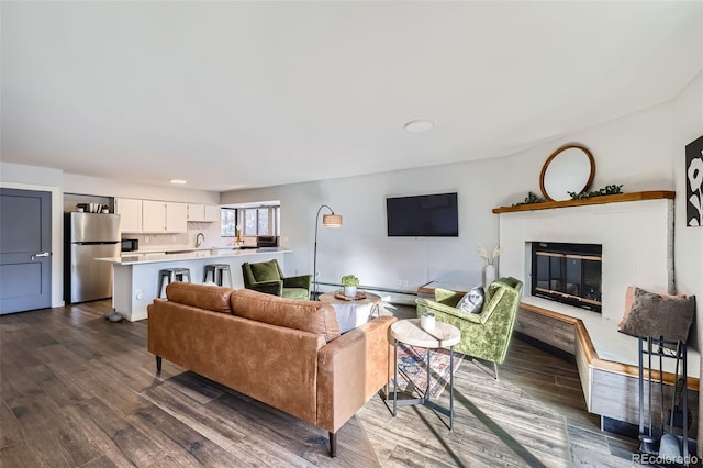 living room featuring a glass covered fireplace, dark wood-type flooring, and a baseboard heating unit