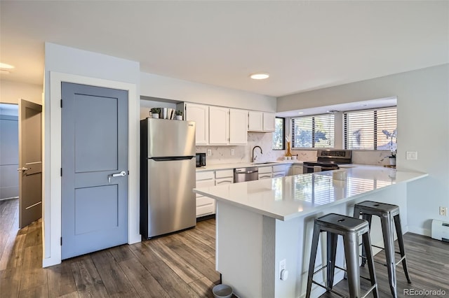 kitchen featuring a breakfast bar, a peninsula, a sink, appliances with stainless steel finishes, and white cabinetry