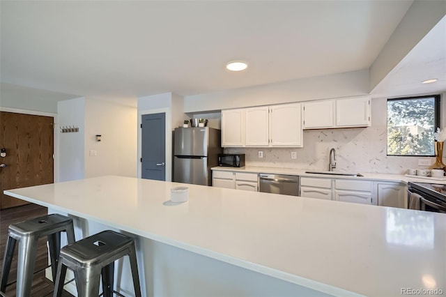 kitchen with a sink, backsplash, white cabinetry, appliances with stainless steel finishes, and a breakfast bar area