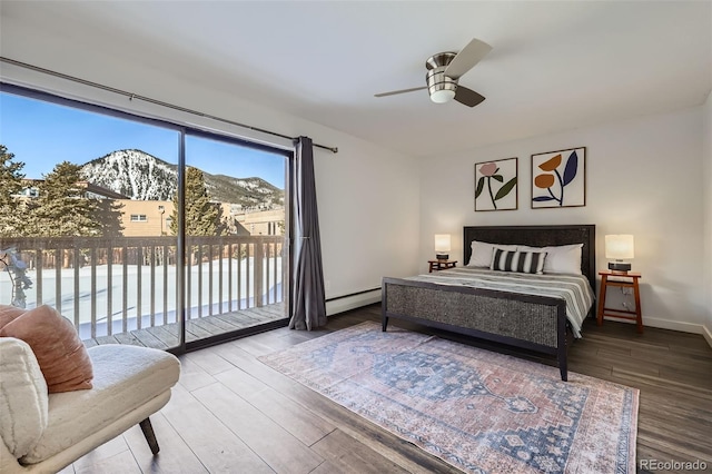 bedroom featuring wood finished floors, baseboards, a baseboard heating unit, access to outside, and a mountain view