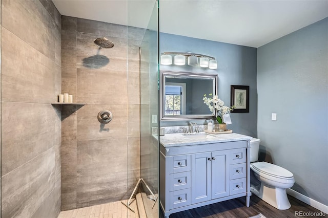 bathroom with baseboards, toilet, tiled shower, wood finished floors, and vanity