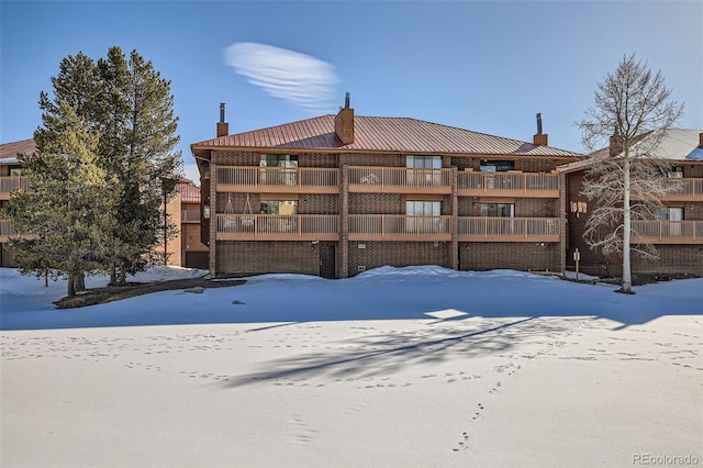 snow covered property with brick siding, a chimney, a standing seam roof, and metal roof