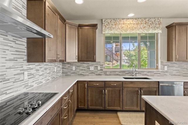 kitchen with light wood-type flooring, sink, wall chimney range hood, backsplash, and stainless steel dishwasher