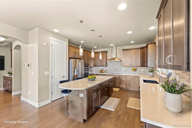 kitchen with sink, wall chimney range hood, stainless steel fridge with ice dispenser, a center island, and light wood-type flooring