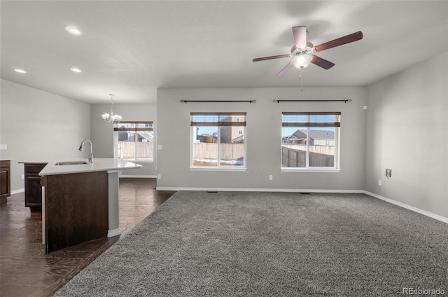 unfurnished living room featuring dark colored carpet, ceiling fan with notable chandelier, and sink