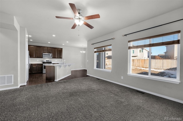 kitchen featuring dark brown cabinets, ceiling fan with notable chandelier, stainless steel appliances, a kitchen island with sink, and dark colored carpet