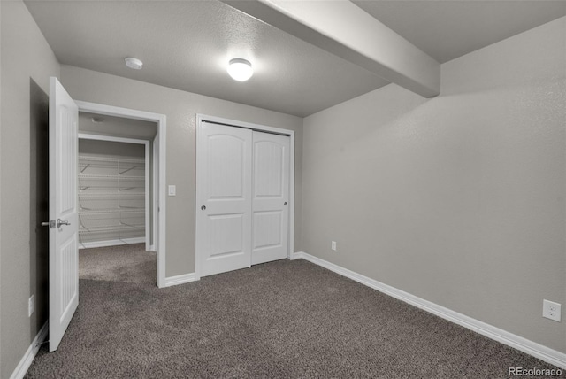 unfurnished bedroom featuring dark colored carpet, beam ceiling, a textured ceiling, and a closet