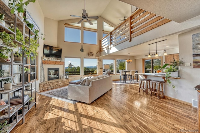 living room with light hardwood / wood-style floors, ceiling fan with notable chandelier, a high ceiling, and a stone fireplace