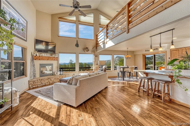 living room with hardwood / wood-style floors, a stone fireplace, a towering ceiling, a textured ceiling, and ceiling fan with notable chandelier