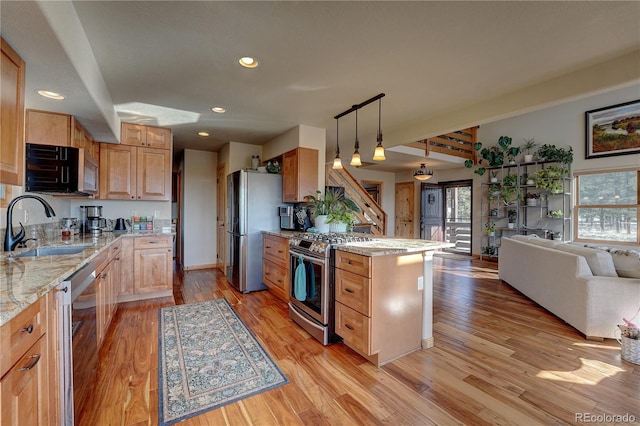 kitchen featuring appliances with stainless steel finishes, hanging light fixtures, light stone countertops, light hardwood / wood-style flooring, and sink