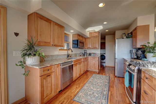 kitchen with light hardwood / wood-style floors, sink, washer / dryer, and stainless steel appliances