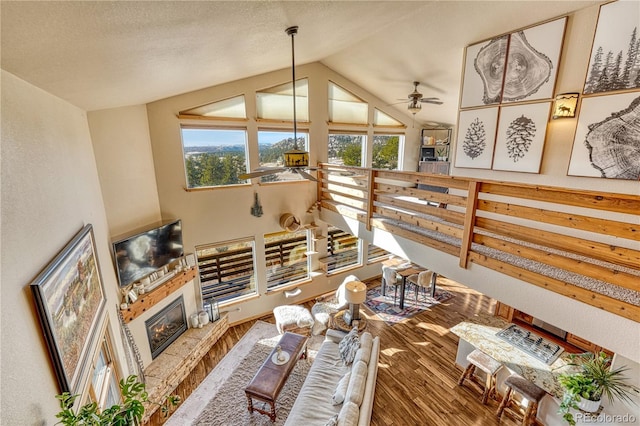 living room with vaulted ceiling, ceiling fan, hardwood / wood-style floors, and a stone fireplace