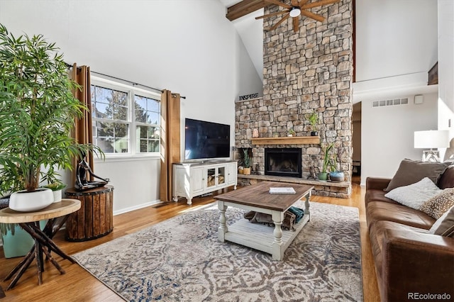 living room featuring a ceiling fan, visible vents, wood finished floors, and a stone fireplace