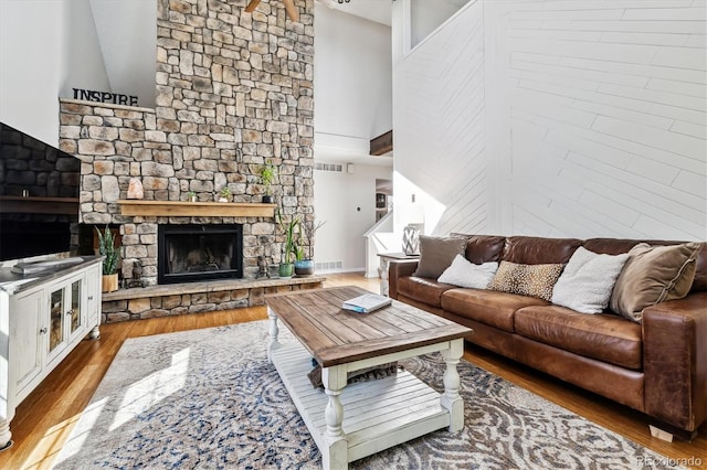 living area featuring visible vents, a stone fireplace, a towering ceiling, and wood finished floors