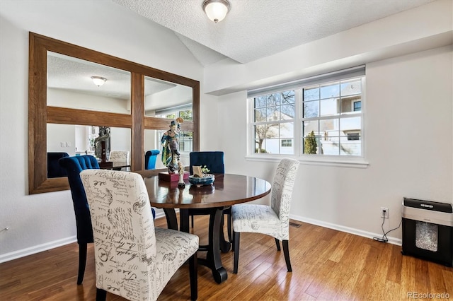 dining area with a textured ceiling, baseboards, and wood finished floors