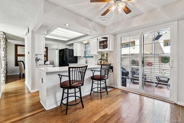 kitchen with light countertops, freestanding refrigerator, white cabinetry, wood finished floors, and a peninsula