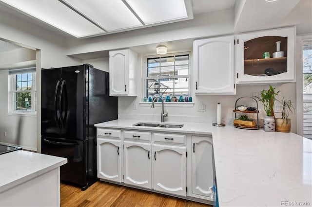 kitchen with light wood-type flooring, freestanding refrigerator, white cabinetry, and a sink