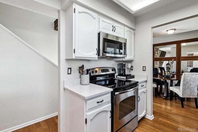 kitchen featuring light countertops, appliances with stainless steel finishes, white cabinetry, light wood-type flooring, and baseboards