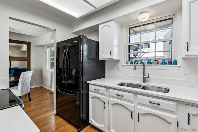 kitchen with black appliances, white cabinetry, light wood finished floors, and a sink