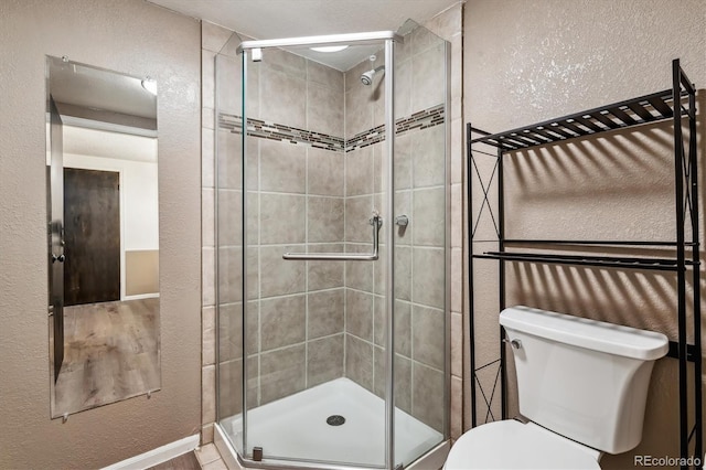 bathroom featuring a textured wall, a stall shower, and toilet