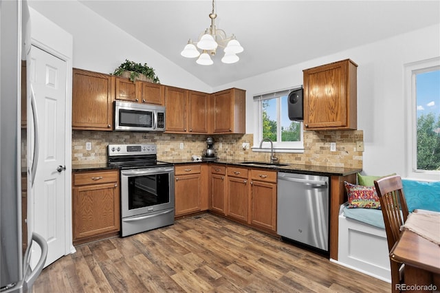 5337 S Ukraine Way, Aurora, CO 80015 - kitchen with stainless steel appliances, dark countertops, lofted ceiling, a chandelier, and brown cabinetry