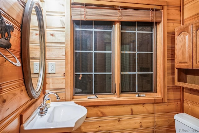 bathroom featuring toilet, wooden walls, and sink