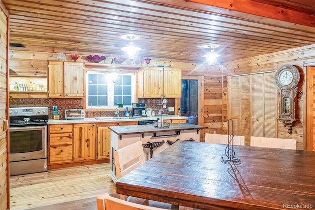 kitchen featuring sink, a kitchen island, wood walls, stainless steel stove, and light wood-type flooring