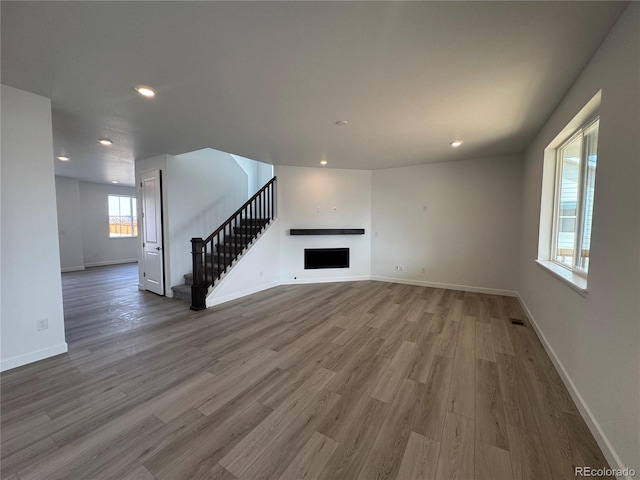 unfurnished living room with stairway, recessed lighting, a fireplace, and wood finished floors