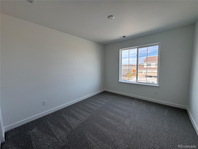 spare room featuring baseboards, visible vents, and dark carpet