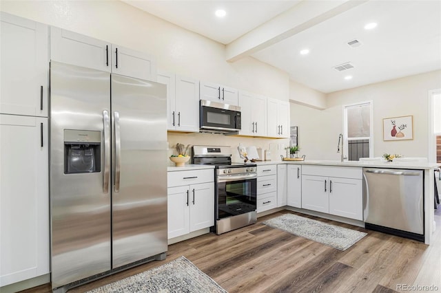 kitchen with appliances with stainless steel finishes, light wood-type flooring, sink, beam ceiling, and white cabinetry