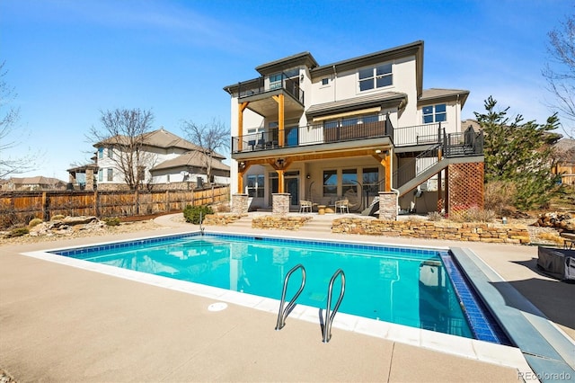 rear view of property featuring a fenced in pool, fence, stairs, a balcony, and a patio