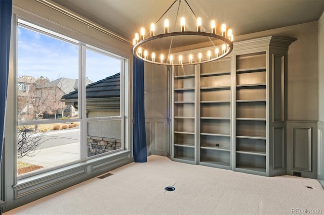 carpeted empty room featuring a chandelier, visible vents, and a decorative wall