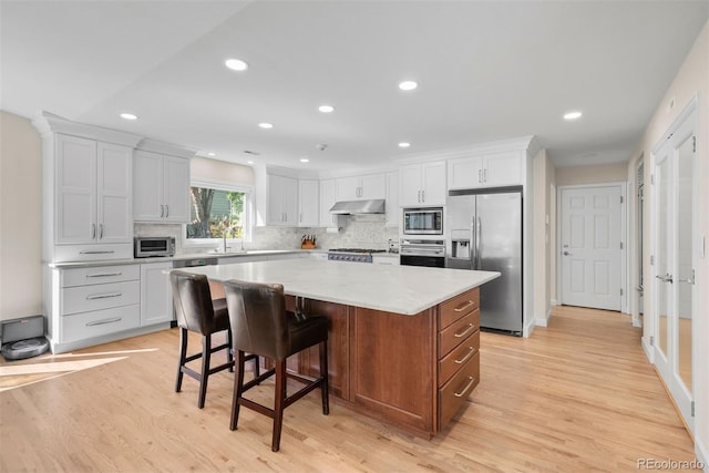 kitchen featuring a center island, stainless steel appliances, sink, light hardwood / wood-style floors, and white cabinetry