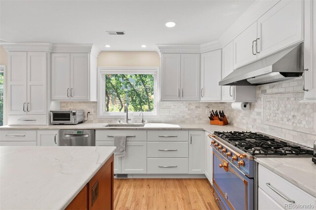 kitchen featuring sink, backsplash, white cabinetry, stainless steel appliances, and light hardwood / wood-style floors