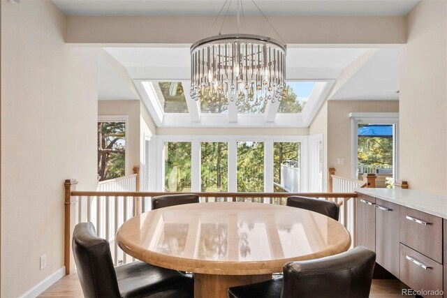 dining area with vaulted ceiling with skylight, an inviting chandelier, and light hardwood / wood-style flooring