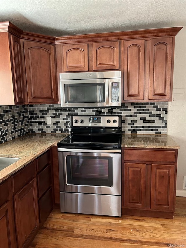 1245 Yates St, Denver, CO 80204 - kitchen with stainless steel appliances, light stone counters, light wood finished floors, backsplash, and a textured ceiling