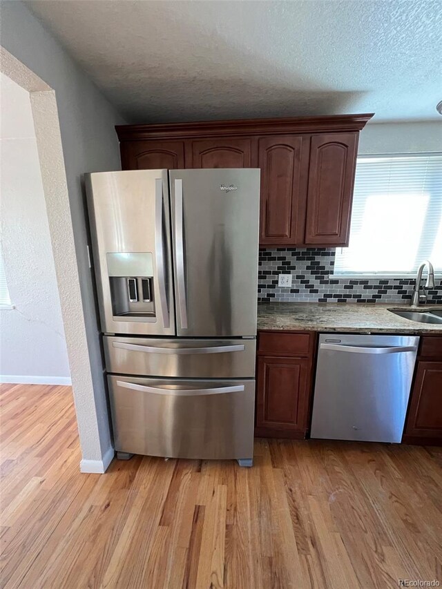 1245 Yates St, Denver, CO 80204 - kitchen with appliances with stainless steel finishes, light wood-style flooring, backsplash, a textured ceiling, and light stone countertops