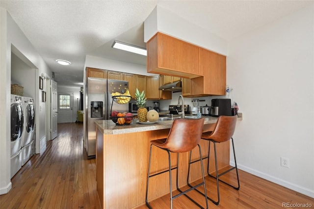 kitchen featuring sink, washer and clothes dryer, stainless steel appliances, a kitchen bar, and kitchen peninsula