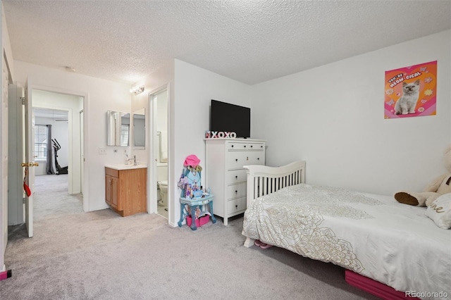 bedroom featuring light carpet, sink, ensuite bath, and a textured ceiling