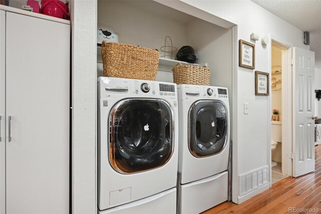 clothes washing area with separate washer and dryer, a textured ceiling, and light hardwood / wood-style floors