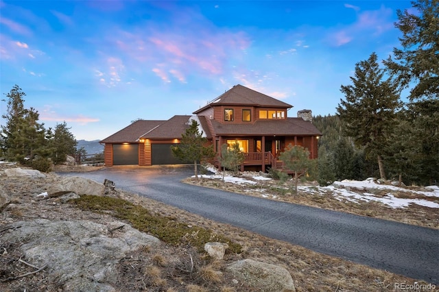 rustic home with a garage, aphalt driveway, a chimney, and log veneer siding